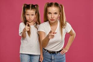 mam en dochter met een grappig paardenstaarten, gekleed in wit t-shirts en blauw denim jeans zijn poseren tegen een roze studio achtergrond. detailopname schot. foto