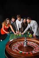 groep van jong mensen achter roulette tafel Aan zwart achtergrond foto