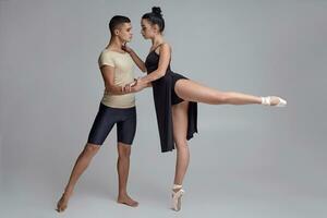 twee atletisch modern ballet dansers zijn poseren tegen een grijs studio achtergrond. foto