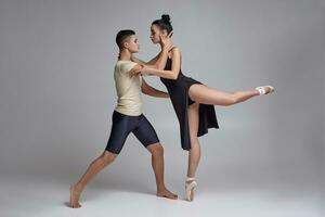 twee atletisch modern ballet dansers zijn poseren tegen een grijs studio achtergrond. foto