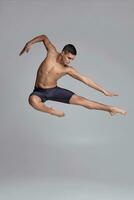 foto van een knap Mens ballet danser, gekleed in een zwart korte broek, maken een dans element tegen een grijs achtergrond in studio.