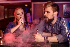 een Mens en vrouw roken elektronisch sigaret in een vapen bar. foto