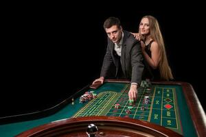 elegant paar Bij de casino wedden Aan de roulette, Aan een zwart achtergrond foto