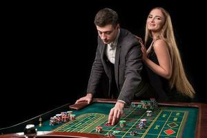 elegant paar Bij de casino wedden Aan de roulette, Aan een zwart achtergrond foto
