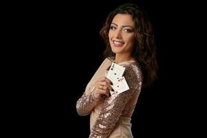 brunette meisje vervelend glimmend jurk poseren Holding twee spelen kaarten in haar hand- staand tegen zwart studio achtergrond. casino, poker. detailopname. foto