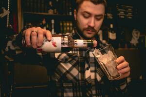 barman gieten grenadine siroop van fles in glas met ijs, voorbereidingen treffen tequila zonsopkomst cocktail foto