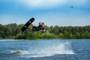 gefocust wakeboarder jumping met bord over- kalmte meer water oppervlakte creëren spatten foto