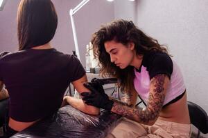 professioneel vrouw tatoeëerder creëren belettering ontwerp Aan arm van cliënt foto