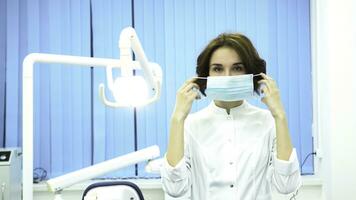 portret van een tandarts zetten Aan de masker op zoek Bij camera Bij de tandheelkundig kliniek. vrouw tandarts assistent staand armen gekruiste met chirurgisch masker Aan haar gezicht. foto
