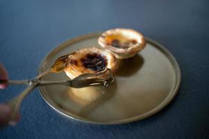 close-up van een hand die een serveertang gebruikt om een heerlijke belemcake, pasteis de belem, te plukken, volgens het Portugese traditionele recept. gastronomie. foto