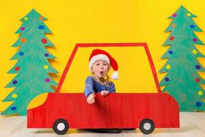 kind met Kerstmis hoed het rijden een auto gemaakt van karton. Kerstmis concept. nieuw jaar vakantie. foto