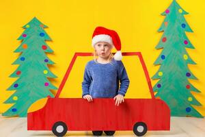 kind met Kerstmis hoed het rijden een auto gemaakt van karton. Kerstmis concept. nieuw jaar vakantie. foto
