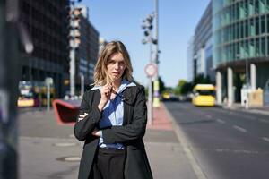 portret van zelfverzekerd bedrijf vrouw in pak, kruis armen Aan borst, op zoek zelfverzekerd in stad centrum, staand Aan straat foto
