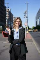 portret van geslaagd jong bedrijf Directeur, zakenvrouw in zwart pak, staand Aan zonnig straat en glimlachen foto