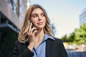 dichtbij omhoog portret van glimlachen verkoopster, geslaagd vrouw manager hebben telefoon telefoongesprek, antwoord telefoon en wandelen Aan straat foto