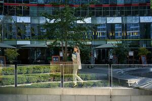 silhouet van jong bedrijf vrouw in beige pak, wandelen in stad centrum, poseren in de buurt kantoor gebouwen, gaan naar werk foto