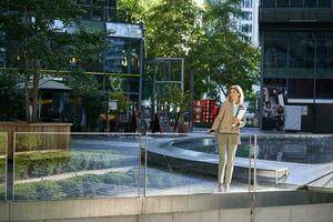 zakelijke vrouw in pak, staand met vertrouwen in beige pak met werken documenten buitenshuis, poseren in stad centrum foto