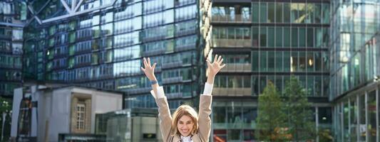 zakelijke vrouw vieren haar zege buiten Aan straat. gelukkig zakenvrouw verhogen handen omhoog en zegevieren van opwinding foto
