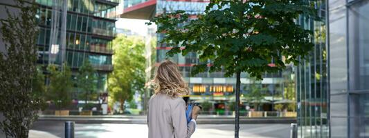 silhouet van jong bedrijf vrouw in beige pak, wandelen in stad centrum, Holding werken documenten en papieren, staand buitenshuis in de buurt kantoor gebouwen foto