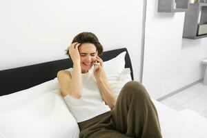 mooi jong modern vrouw pratend naar vriend, aan het liegen in bed en roeping iemand Aan telefoon, resting Bij huis, chatten foto