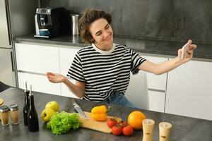 portret van mooi jong vrouw, voedsel blogger opname video van haar Koken in de keuken, tonen maaltijd ingrediënten, voorbereidingen treffen een maaltijd Aan camera, gebruik makend van smartphone voor leven streaming foto