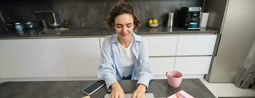 top visie van zakenvrouw werken van huis. meisje studies van een afstand Aan laptop, zit in keuken en looks Bij scherm, horloges webinar, online Cursus foto