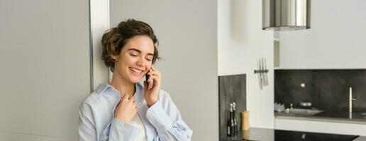 portret van vrouw pratend Aan mobiel telefoon en lachend, uitgeven tijd Bij huis, heeft telefoon gesprek, antwoorden een telefoontje foto