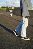 bijgesneden schot van tiener schaatser meisje, handen Holding longboard, wandelen met skateboard Aan beton weg foto