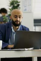 bedrijf ondernemer voorbereidingen treffen Product lancering strategie terwijl werken Aan laptop in bedrijf kantoor. Arabisch zakenman planning afzet Onderzoek Aan computer Bij werkplaats in coworking ruimte foto