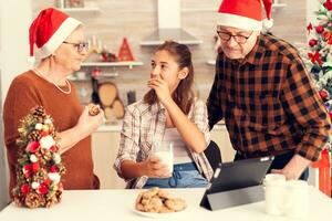 multi generatie familie genieten van toetje Aan Kerstmis dag. gelukkig kind vervelend de kerstman hoed aan het eten heerlijk koekjes van grootouder terwijl vieren winter vakantie met hen. foto