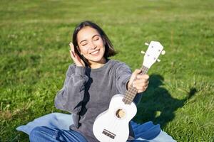 glimlachen Aziatisch meisje met ukelele, spelen in park en zingen, levensstijl concept foto