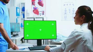 assistent geven dokter geduldig röntgenstraal terwijl ze is werken Aan computer met kopiëren ruimte groen scherm beschikbaar in ziekenhuis kastje. medisch in wit jas werken Aan toezicht houden op met chroma sleutel in kliniek kabinet naar controleren geduldig diagnostiseren. foto