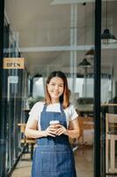 jong vrouw hangende een Welkom teken in voorkant van een koffie winkel. mooi serveerster of gastvrouw Holding een tablet voorbereidingen treffen in een restaurant. foto