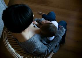 jong vrouw borstvoeding geeft haar weinig zoon terwijl zittend in een knus fauteuil foto