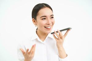 professioneel zakenvrouw, Aziatisch dame glimlacht, spreekt Aan luidsprekertelefoon, records stem bericht Aan smartphone, wit achtergrond foto