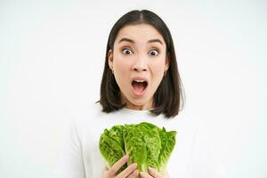 vrouw met geschokt gezicht, schreeuwt, houdt groente, rauw voedsel, eet kool Aan eetpatroon, wit achtergrond foto