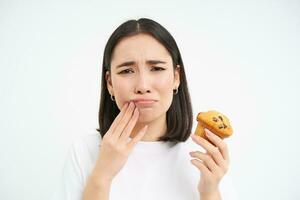 dichtbij omhoog portret van Aziatisch vrouw met tandenstoker, looks Bij koekje, te zoet nagerecht, kan niet eten, wit achtergrond foto