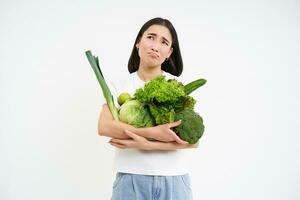 vrouw met walgde gezicht, Holding groenten, groen biologisch voedsel, heeft een hekel aan diëten en ontgiften, wit achtergrond foto