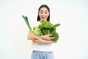 portret van mooi, gezond jong vrouw, Holding groen groenten, veganistisch geniet groen oranisch voedsel, staand over- wit achtergrond foto