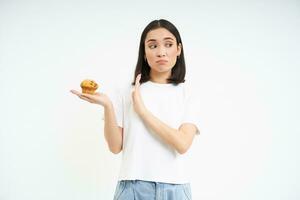 schattig Aziatisch meisje met zullen stroom, weigert de koekje, blijft Aan eetpatroon, geïsoleerd Aan wit achtergrond foto