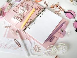 bovenaanzicht van een roze planner met schattig briefpapier. roze glamourplanner met een wit paspopbeeldje. planner met open pagina's op een witte achtergrond en met mooie accessoires pennen, knopen, pinnen. foto