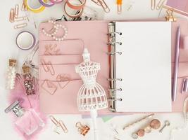 bovenaanzicht van een roze planner met schattig briefpapier. roze glamourplanner met een wit paspopbeeldje. planner met open pagina's op een witte achtergrond en met mooie accessoires pennen, knopen, pinnen. foto