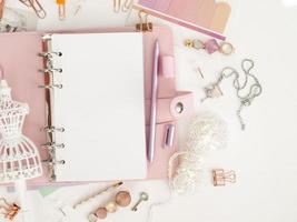 bovenaanzicht van een roze planner met schattig briefpapier. roze glamourplanner met een wit paspopbeeldje. planner met open pagina's op een witte achtergrond en met mooie accessoires pennen, knopen, pinnen. foto