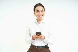 mooi zakelijke vrouw, Holding smartphone in handen en op zoek terzijde Bij bedrijf bedrijf banier, staand geïsoleerd Aan wit achtergrond foto