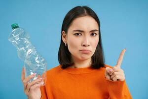 echt Aziatisch vrouw vertelt naar recyclen, shows plastic fles en dringt aan op soort en verzamelen verspilling naar recycling centra, blauw achtergrond foto