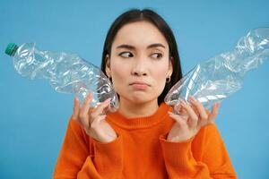 denken boos meisje, shows twee flessen, recycling plastic, gaat groente, herbruikbaar afval, blauw achtergrond foto