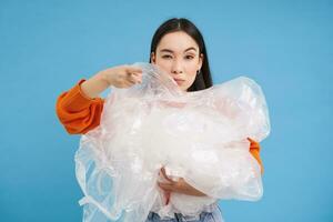 streng jong vrouw vrijwilliger, tonen plastic afval, aanmoedigen naar recyclen, blauw achtergrond foto