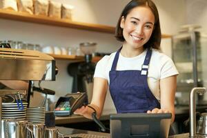 klein bedrijf en mensen. glimlachen Aziatisch vrouw barista, werken in cafe, geven pos terminal, credit kaart machine, verwerken bestellen foto