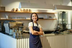 portret van glimlachen Aziatisch ondernemer, onafhankelijk koffie winkel baasje, vervelend schort, werken in cafe, vervelend schort foto