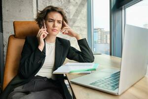 portret van vrouw hebben echt gesprek over- de telefoon. zakenvrouw werken in haar kantoor, beantwoorden telefoon telefoontje met echt, bezorgd gezicht uitdrukking foto